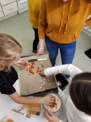 Lapset pilkkovat tomaatteja ja kinkkuja ruokakerhossa.