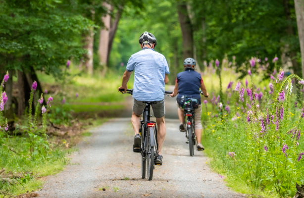 en man och en kvinna cyklar ute på en grusväg i naturen bland blommor. Mies ja nainen pyöräilevät soratietä pitkin luonnossa kukkien keskellä