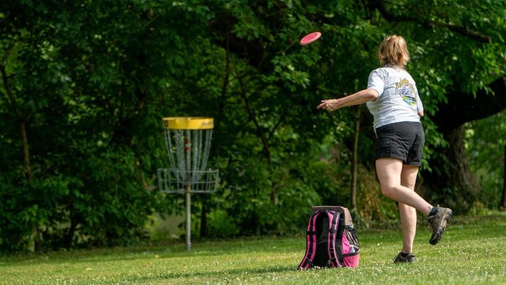 Nainen heittää frisbeetä puistossa.
